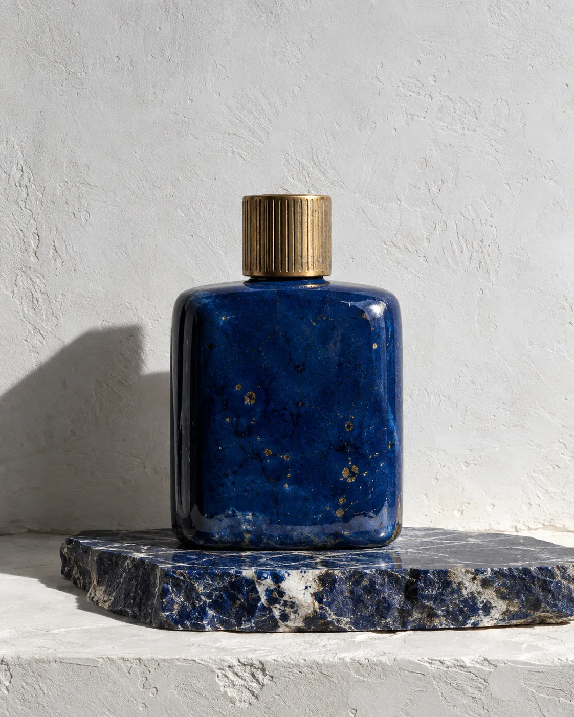 Khepri flacon in lapis-blue glaze on a slab of raw lapis lazuli, hard sun on a white wall